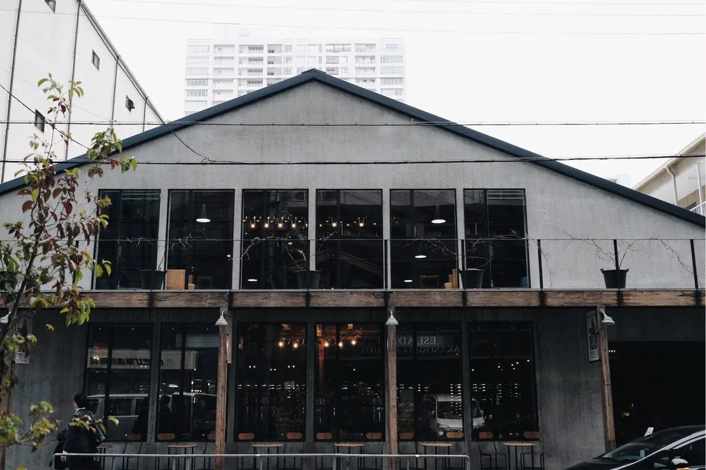 modern industrial building with large windows, wooden deck, and urban apartment towers behind., takamura wine & coffee roaste