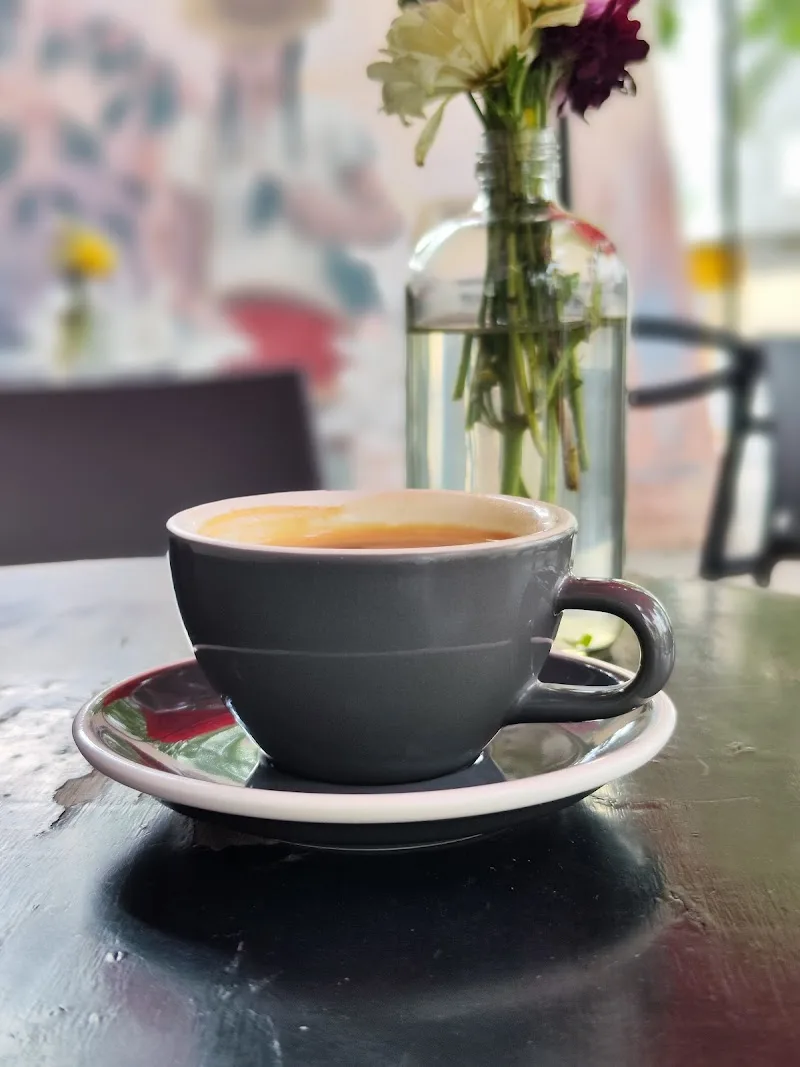 black coffee cup on saucer with fresh flowers in glass vase behind., taller de espresso, guadalajara