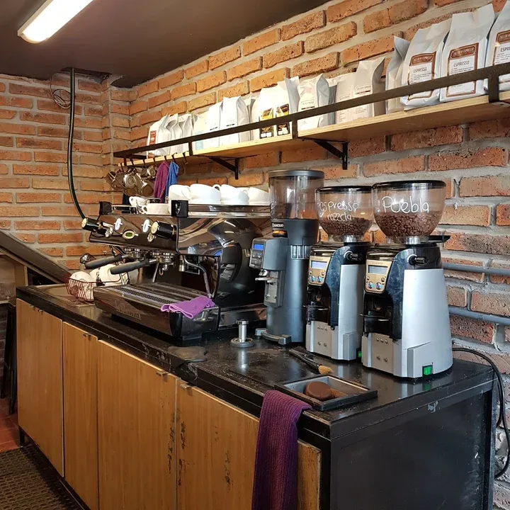 coffee shop counter with espresso machine, grinders, and storage shelves against brick wall., taller de espresso, guadalajara