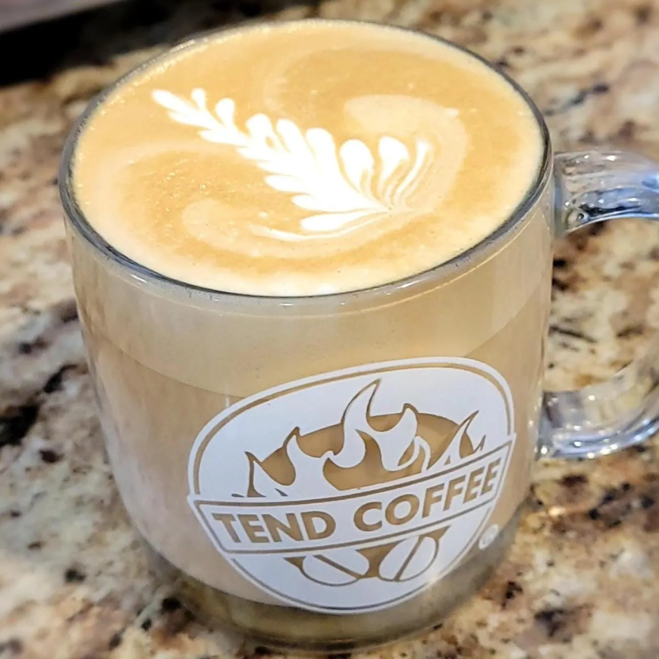 latte with leaf latte art in tend coffee branded glass cup on speckled countertop., tend coffee, new york