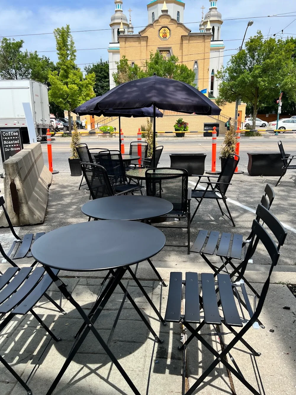 outdoor patio seating with black umbrellas and tables near yellow church building., terminal 3 coffee roasters - lake shore, 