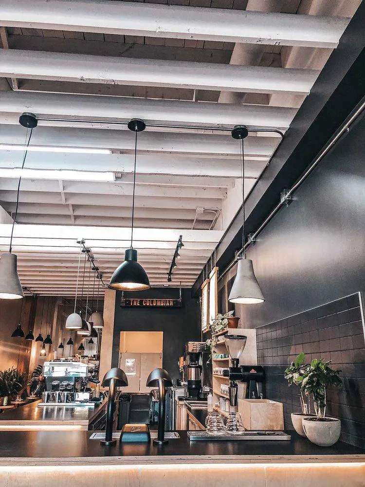 modern industrial coffee shop interior with pendant lighting and exposed ceiling beams., the colombian coffee bar & roastery-