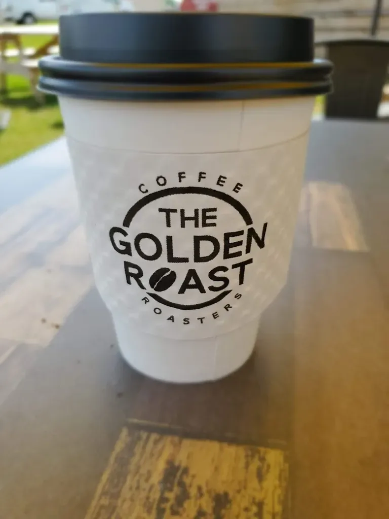 coffee cup from the golden roast roasters with black lid on wooden table outdoors., the golden roast coffee house & roaster, 