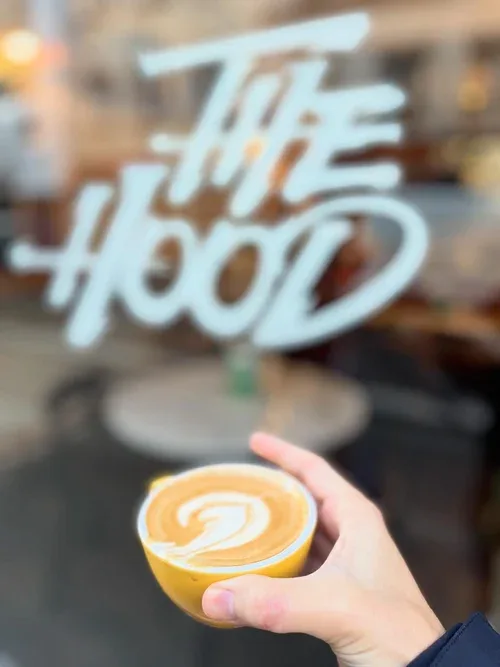 hand holding latte with latte art in front of café storefront window., the hood, paris