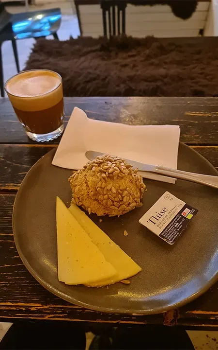 espresso drink beside plate with pastry, cheese wedge, and butter packet., the little yellow coffee bar, copenhagen