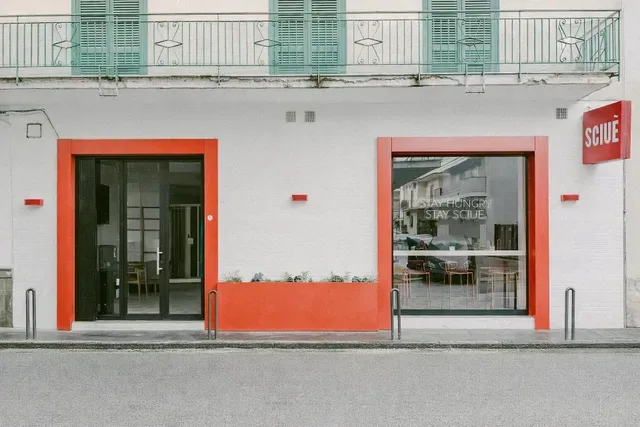 modern storefront with red-framed entrance, white facade, and green balconies above., the sign 2.0 - medieval fantasy pub & c