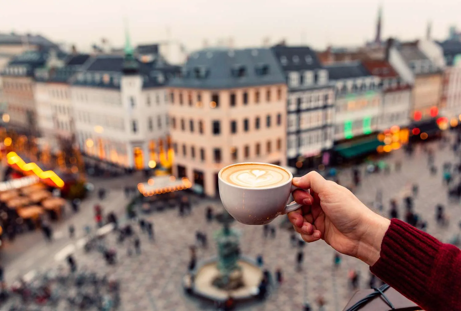 hand holding latte with latte art overlooking european city square., the spot, copenhagen