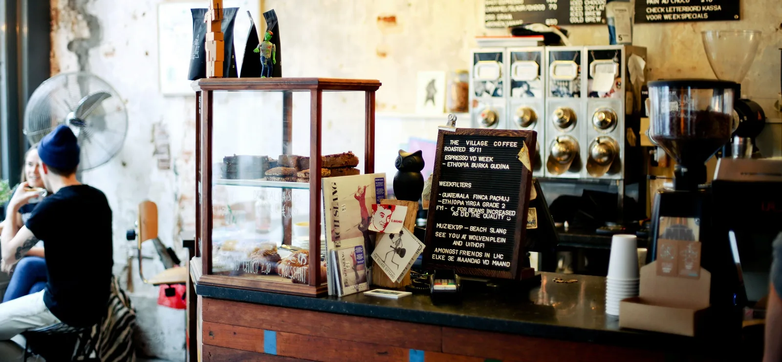 artisanal coffee shop counter with menu board, pastries, and brewing equipment., the village coffee & music, utrecht
