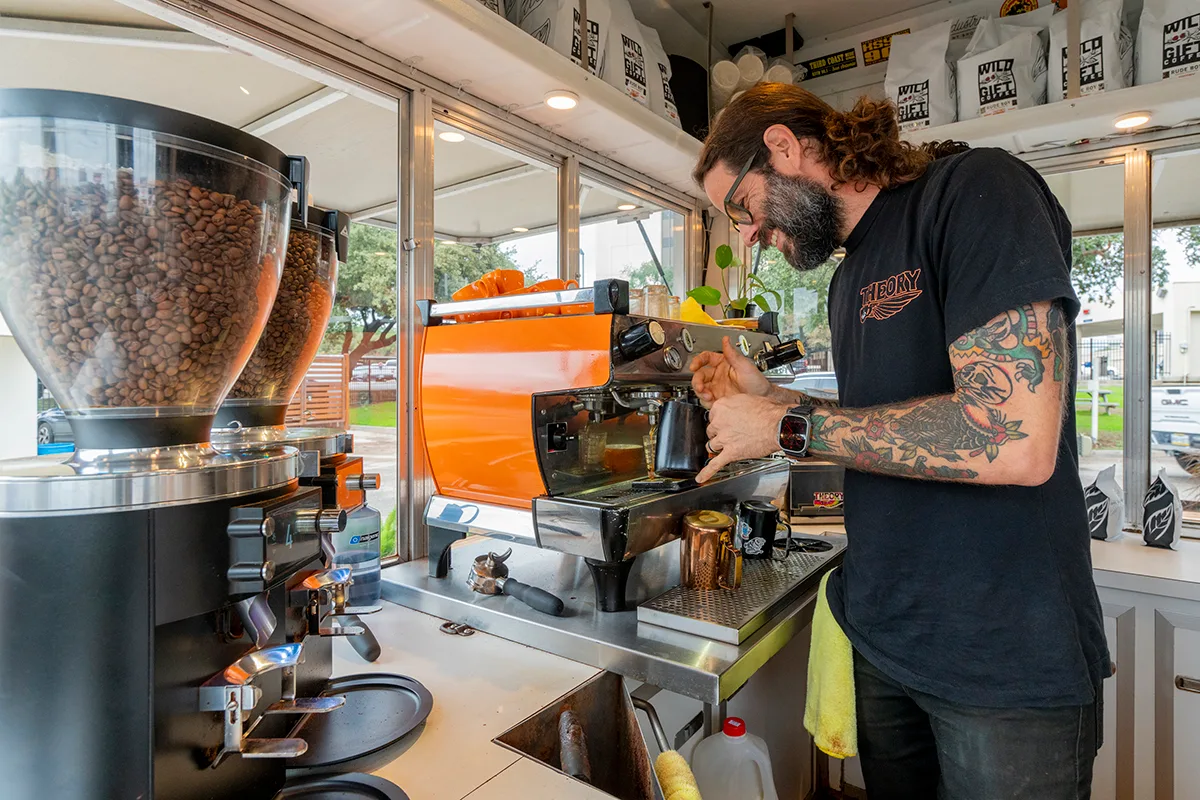 bearded barista operates espresso machine in bright coffee shop with orange grinder., theory coffee company, san antonio