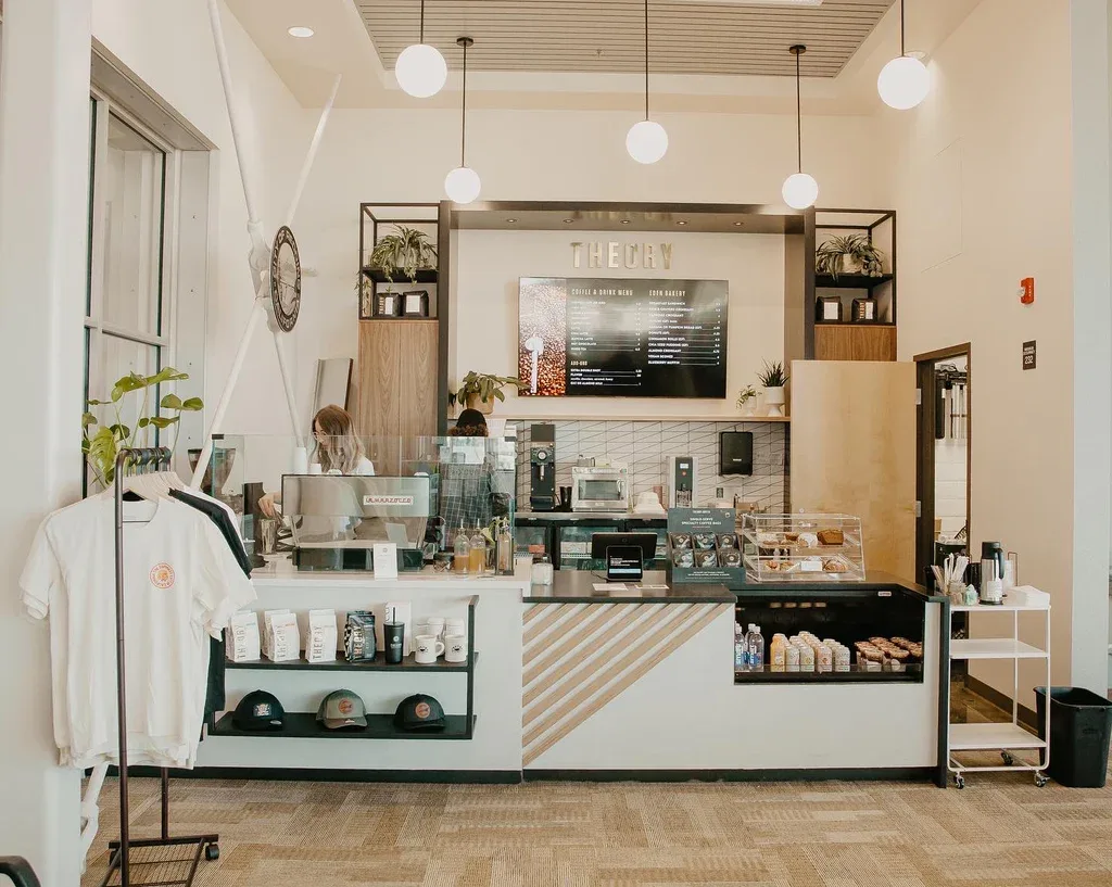 modern coffee shop counter with "theory" signage, pendant lights, and retail merchandise display., theory coffee roasters, re