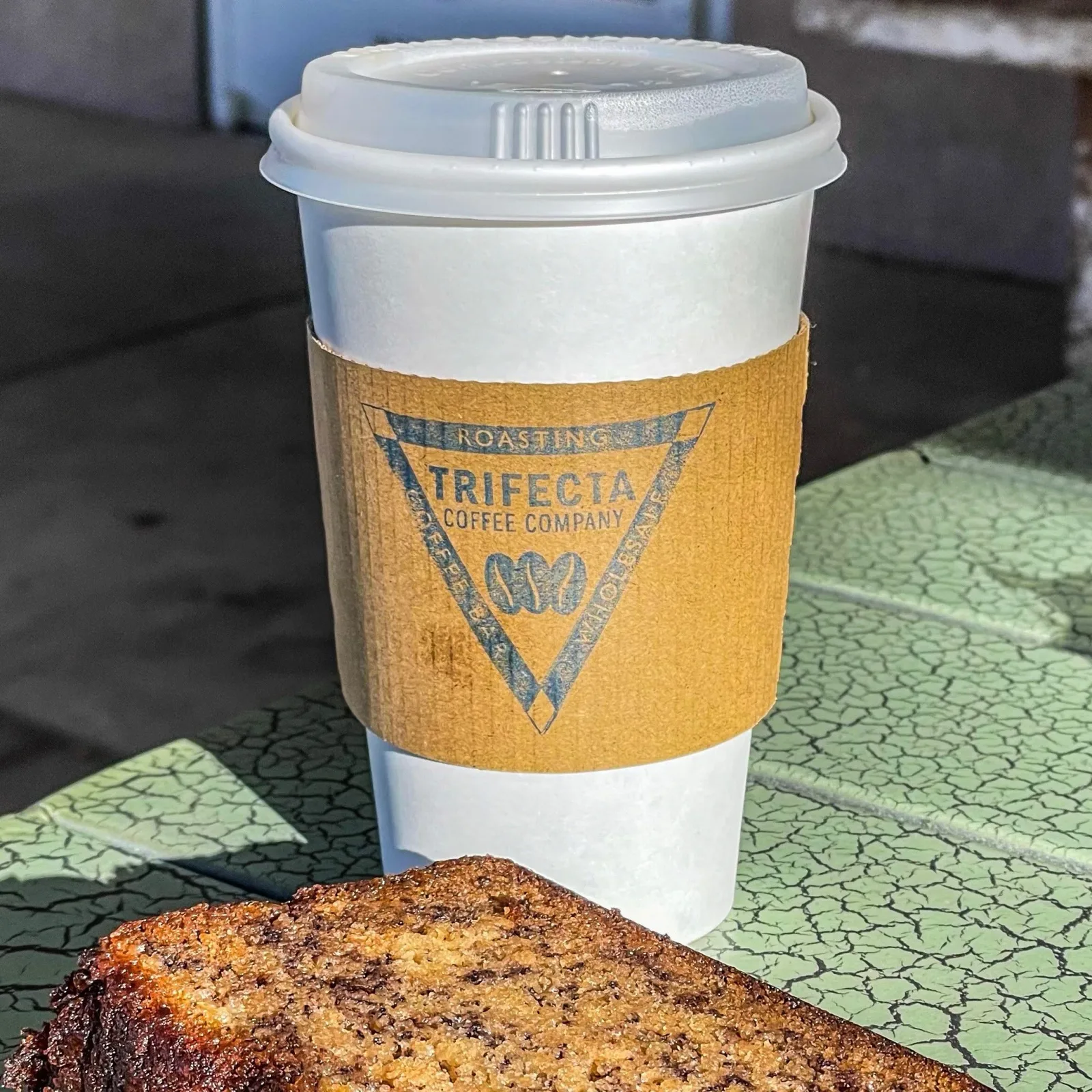 trifecta coffee company cup with pastry on textured green surface., trifecta coffee company, albuquerque
