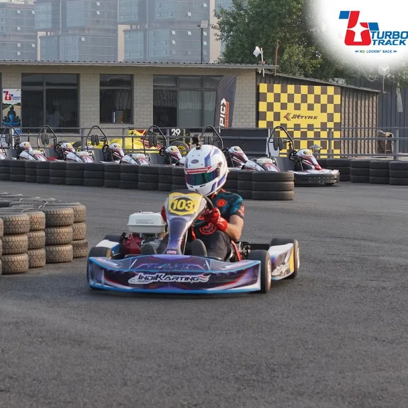 go-kart racer in helmet on track with yellow barriers and other karts., turbo track, gurugram