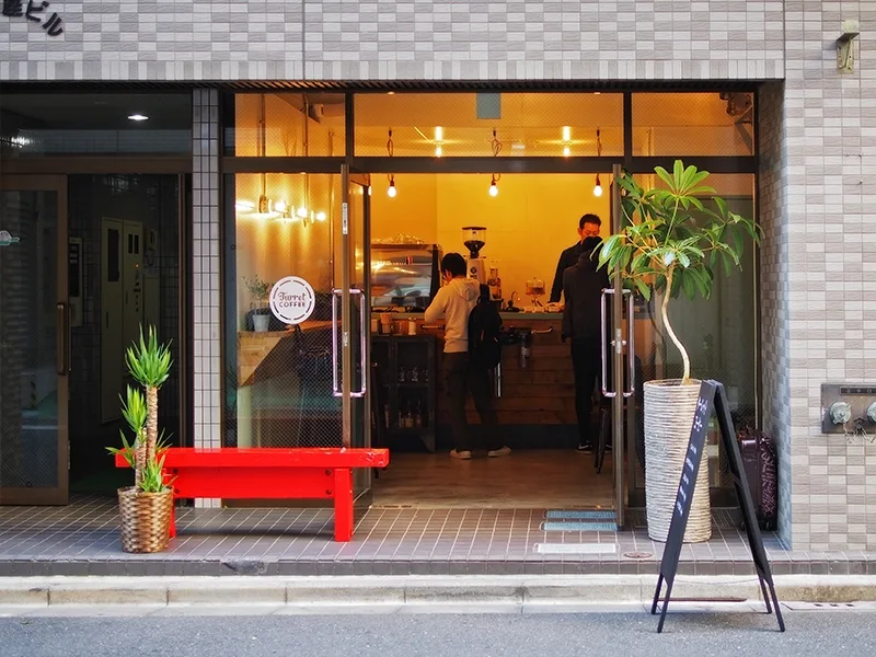 modern café storefront with warm lighting, red bench seating, and potted plants outside., turret coffee tsukiji, tokyo