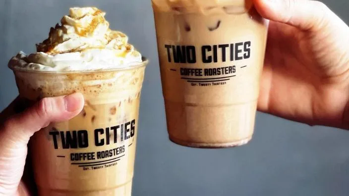 two iced coffee drinks in branded cups, one topped with whipped cream and caramel., two cities coffee roasters, fresno