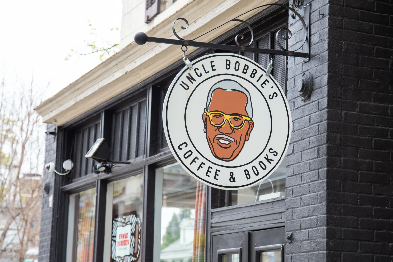 uncle bobbie's coffee and books storefront with hanging sign featuring illustrated man with glasses., uncle bobbie's coffee &