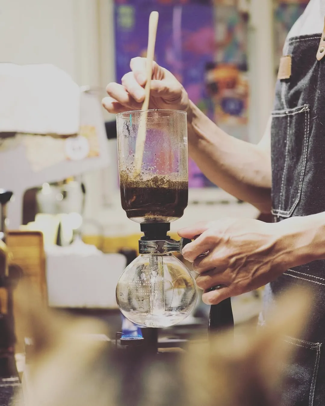 person preparing pour-over coffee using glass dripper and wooden stirrer., uni cafe, taipei