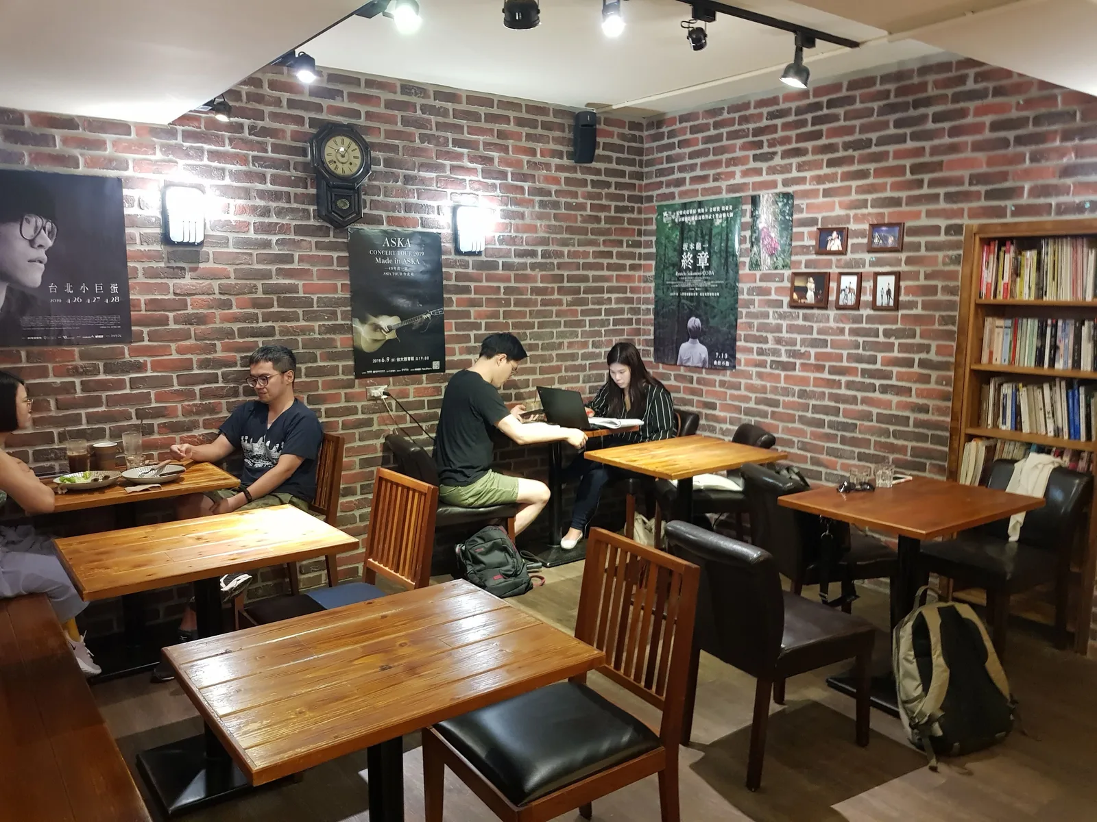 brick café interior with wooden tables, students studying, bookshelves, and posters., uni cafe, taipei