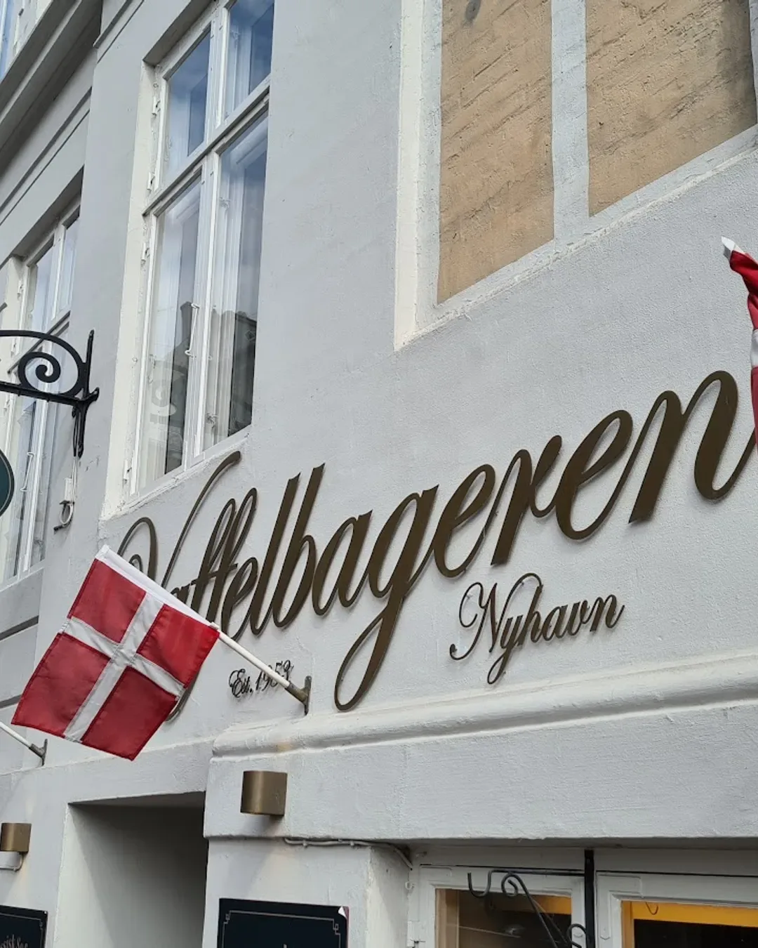 danish flag and storefront signage for hellbageren nyhavn bakery on white building., vaffelbageren nyhavn, copenhagen