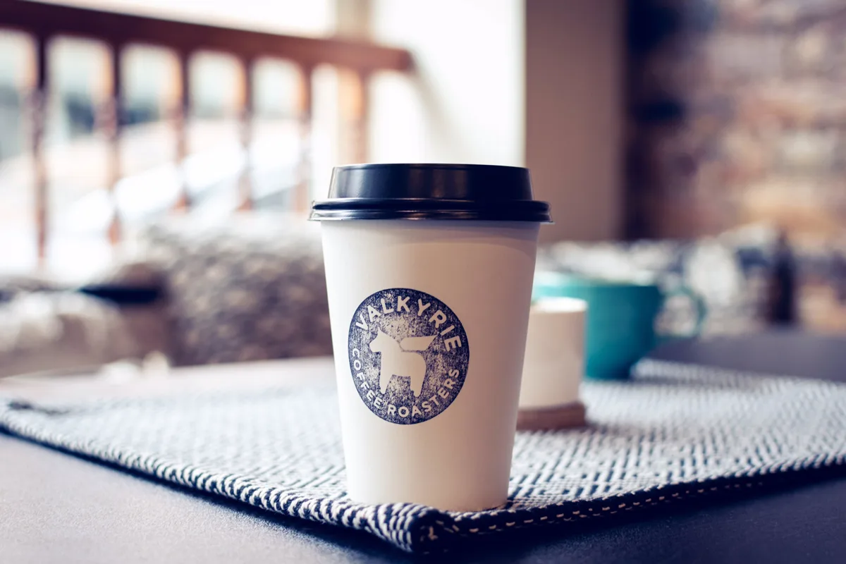 white coffee cup with dark lid and circular logo on textured mat indoors., valkyrie coffee roasters, chester