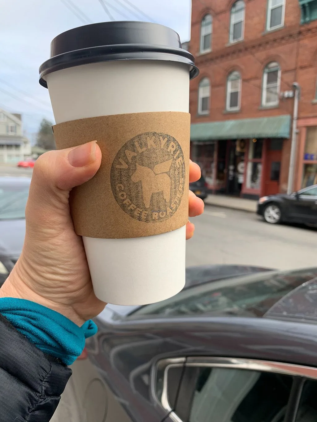 hand holding coffee cup with cork sleeve and circular logo on street., valkyrie coffee roasters, chester