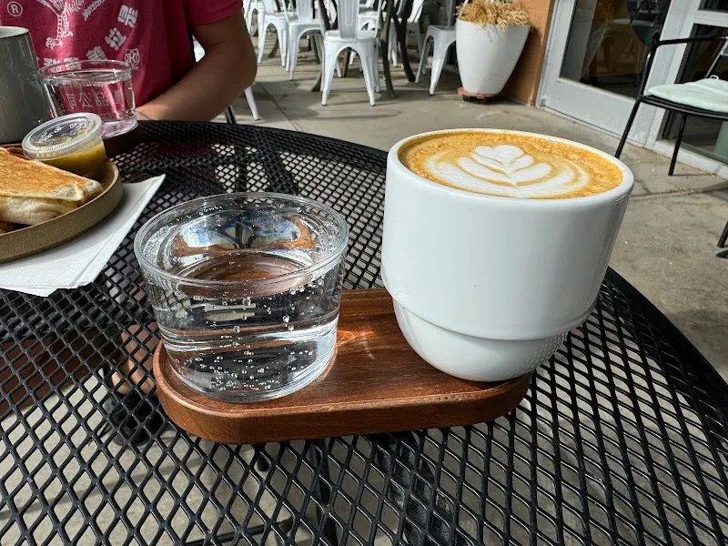 outdoor café table with latte art coffee, water glass, and pastries on perforated surface., verb coffee roasters, boulder