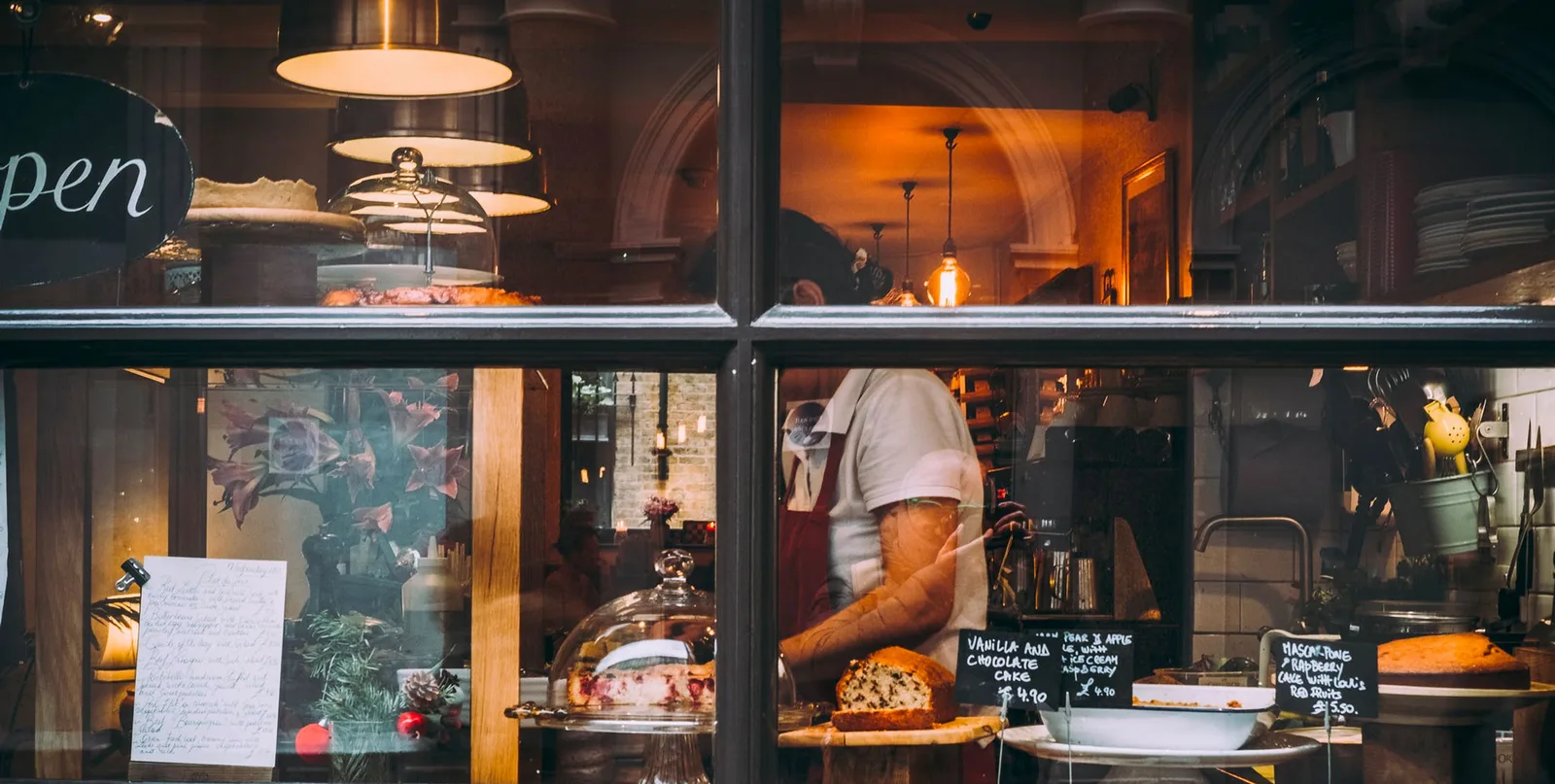 bakery storefront window displaying pastries, cakes, and a baker at work inside., verdensbakeriet oslo, oslo
