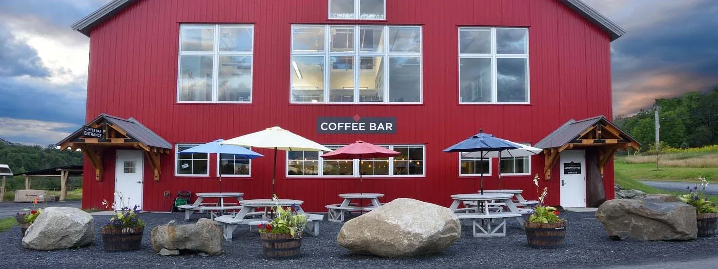 red coffee bar building with picnic tables, umbrellas, and large boulders., vermont artisan coffee and tea, waterbury