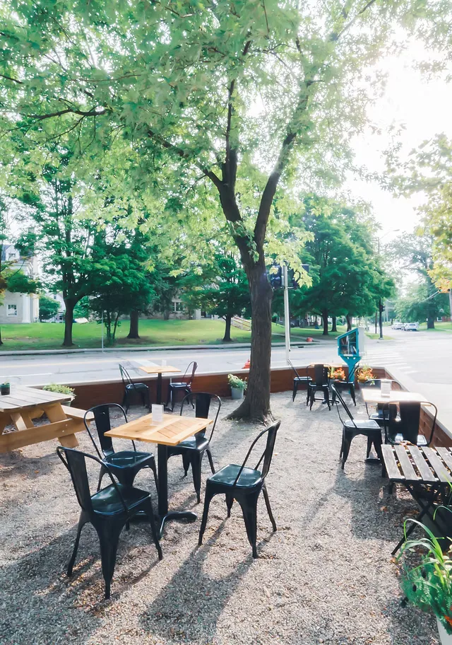outdoor park seating area with wooden tables, black metal chairs, and large trees., vertex coffee roasters, ann arbor
