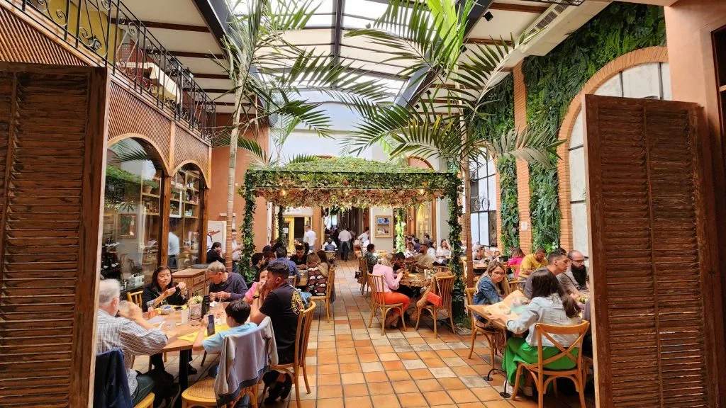 lush indoor dining space with ivy-covered walls, palm trees, and patrons seated at tables., vila dalí gastronomia, são paulo