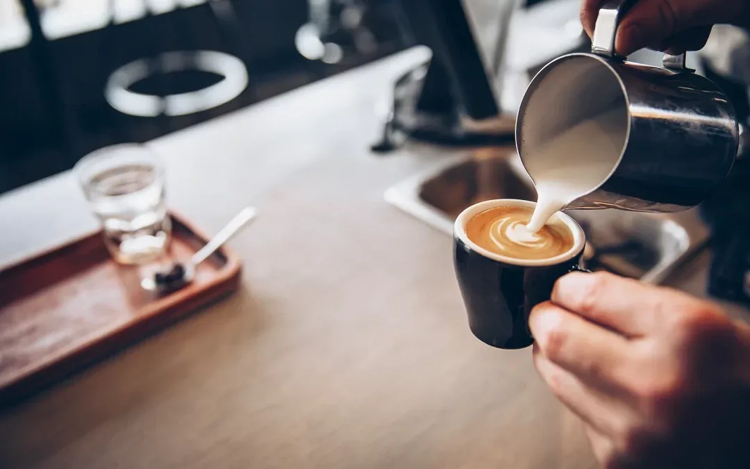 barista pouring steamed milk into espresso, creating latte art design., walden's coffeehouse, reno
