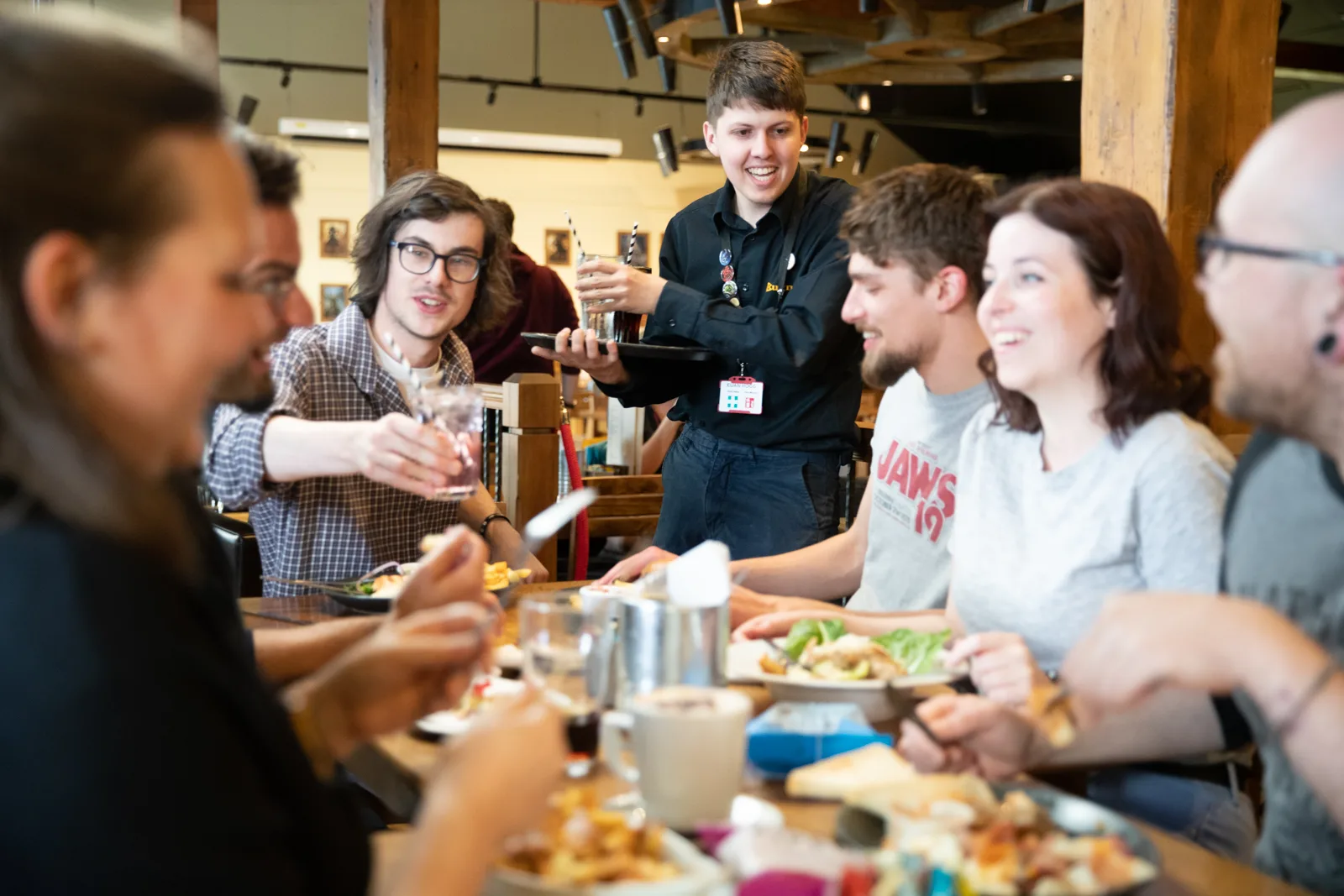group of young people eating and socializing together at a wooden table indoors., warhammer world, nottingham