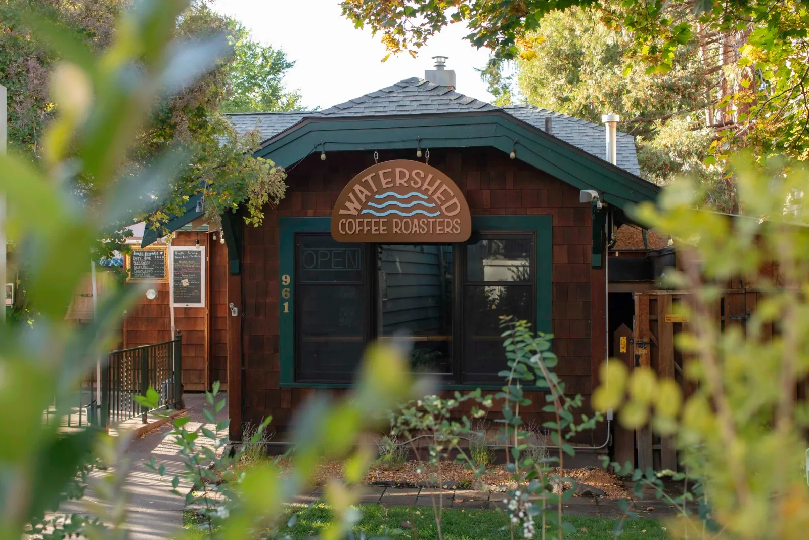 watershed coffee roasters storefront nestled among green foliage and trees., watershed coffee roasters, bend