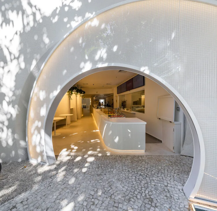 curved white archway entrance to modern interior space with warm lighting., we coffee ibirapuera, são paulo