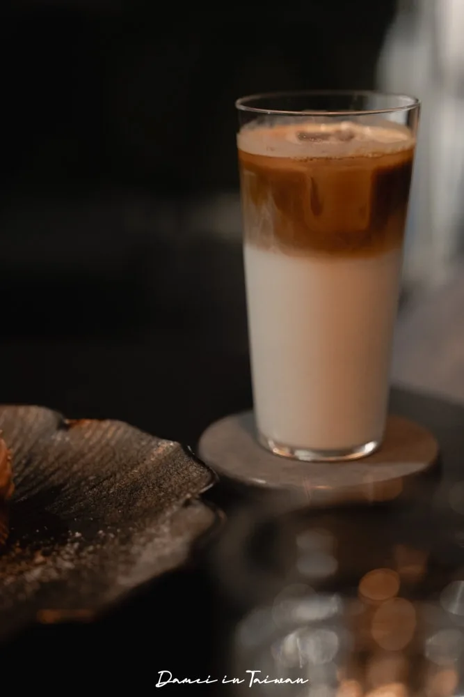 iced coffee with milk in a tall glass on wooden coaster, dark background., what’s life coffee roasters, taipei