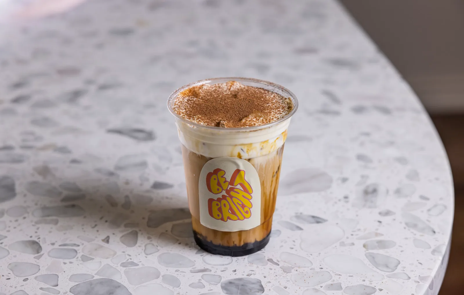 tiramisu-topped iced coffee drink on speckled white table with branded cup sleeve., yala coffee, los angeles