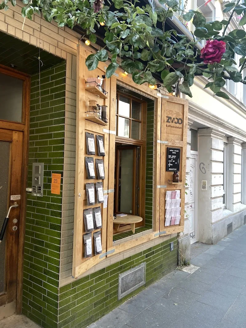 small storefront with green brick, wooden frame, and climbing roses overhead., zwoo kaffeeröster ⎮ kaffeefenster, cologne
