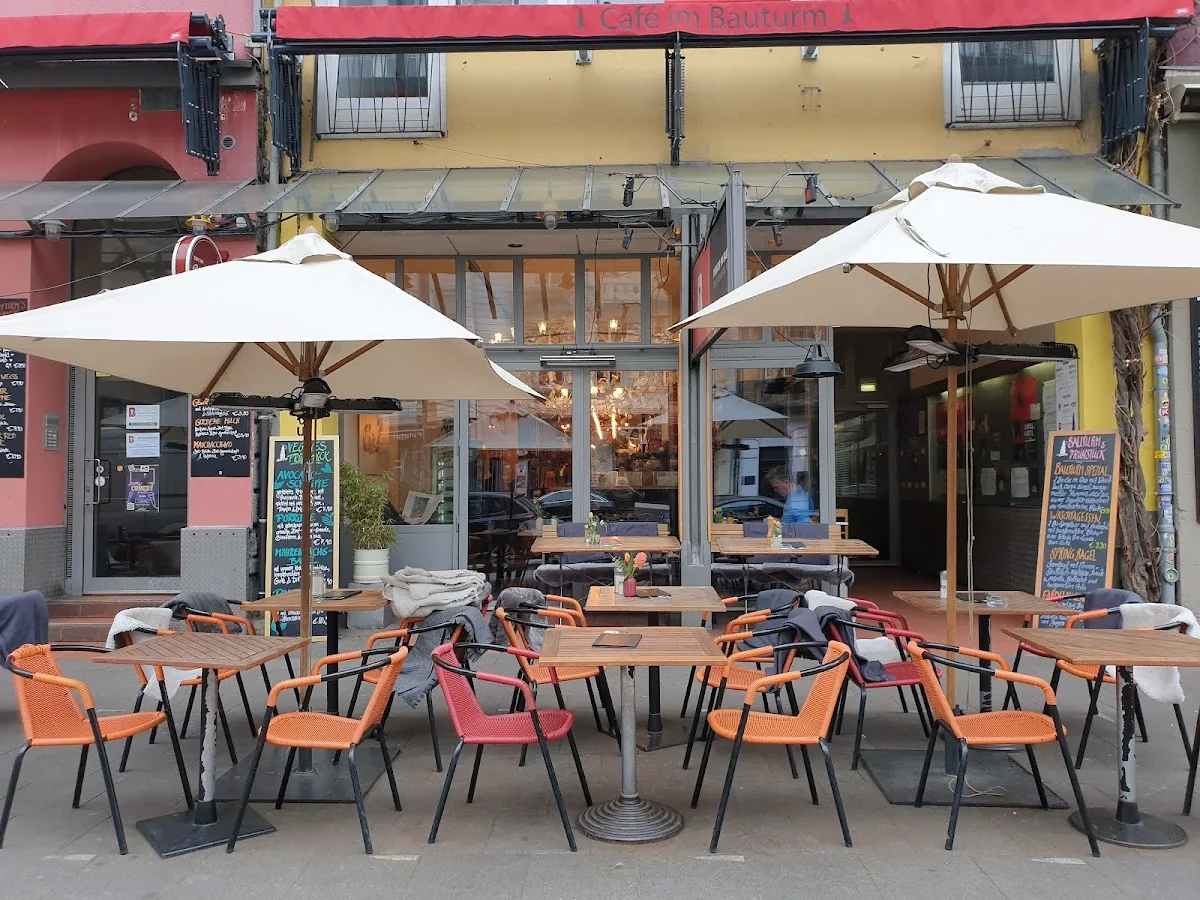 outdoor café terrace with orange chairs, white umbrellas, and wooden tables., zwoo kaffeeröster ⎮ kaffeefenster, cologne